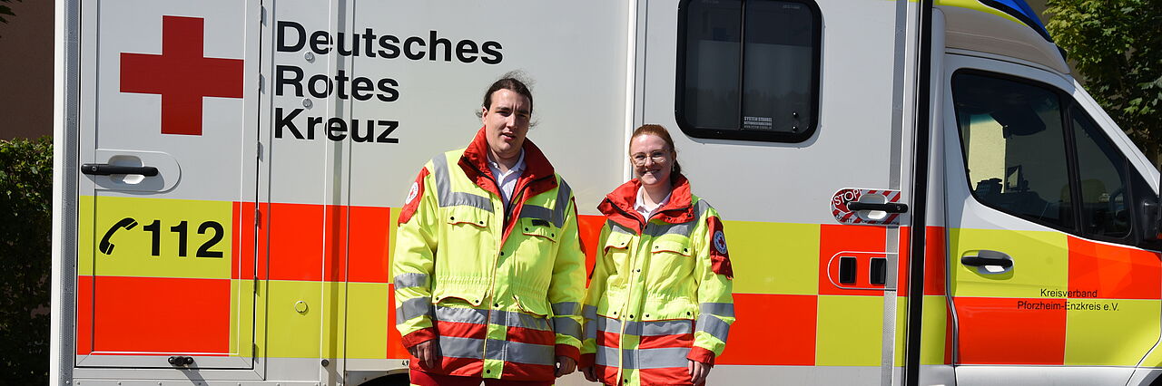 Rettungsdienst_JS Zwei Rettungsdienstmitarbeiter stehen vor einem Rettungswagen.