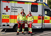 Zwei Rettungsdienstmitarbeiter stehen vor einem Rettungswagen.