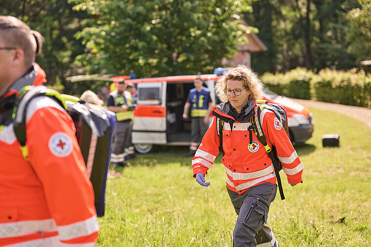 Sanitätshelfer in EInsatzkleidung laufen über Wiese.