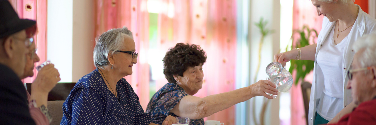 ServiceleistungsgGmbH DRK-Mitarbeiterin schenkt Seniorinnen und Senioren frisches Wasser ein.
