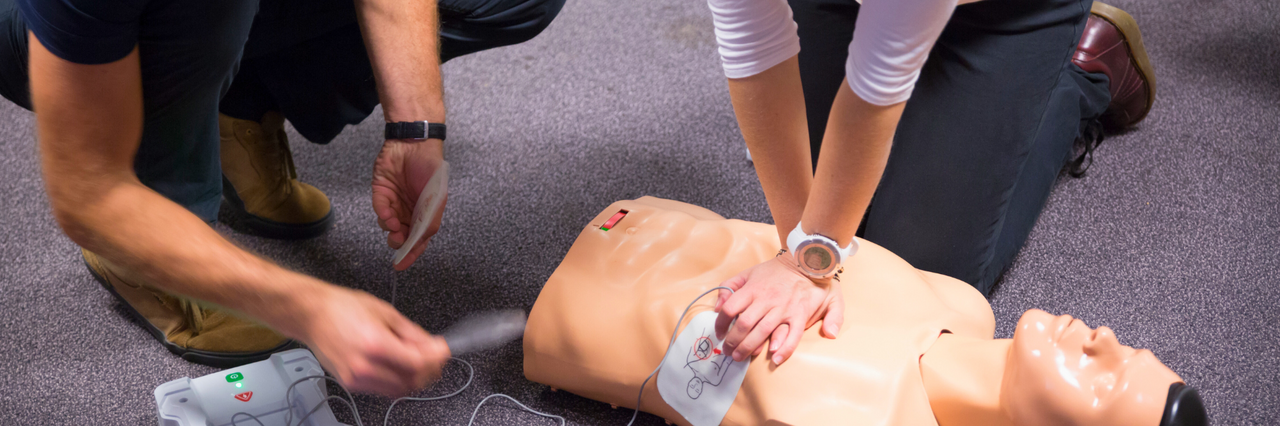AED-Kurs Personen üben an einer Puppe die Wiederbelebung mit einem AED.