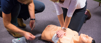 Personen üben an einer Puppe die Wiederbelebung mit einem AED.